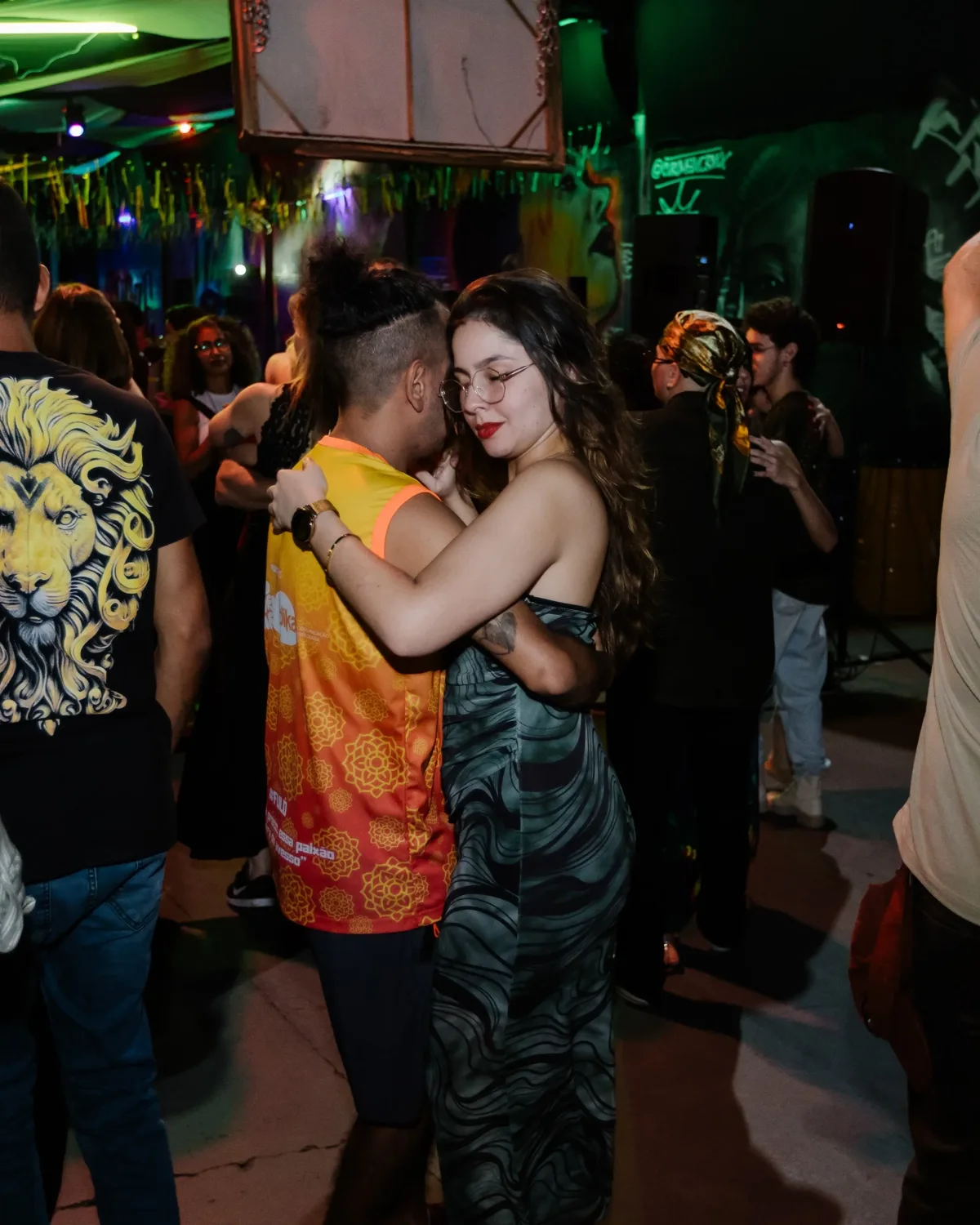 Casal dançando forró abraçado na pista, cercado por outros pares, em uma noite do MovimentAê